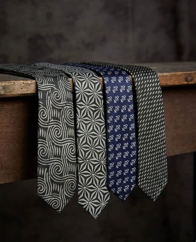 A row of hand block-printed silk neckties draped over a wooden beam
